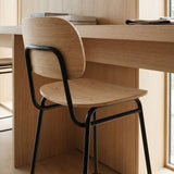 sackit wood bar stool with curved backrest and black metal frame tucked beneath a wooden desk in a warm Nordic interior