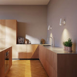 White Expo Wall light with aluminum base and warm glow mounted on a wall.