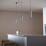 Polished aluminum Expo Pendant light with a slim cylindrical shape and long cord hanging indoors.