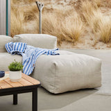 Beige outdoor lounger by sackit with a blue striped throw beside a wooden coffee table in a calm Nordic garden setting