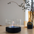 Black stainless steel SACKit Bio Lamp with heat-resistant glass and ethanol container on a wooden table outdoors.