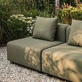 sackit outdoor two seater lounge sofa in olive green fabric with cushions on a gravel patio surrounded by lush Nordic garden planting