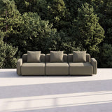 sackit three seat outdoor lounge sofa in taupe with three cushions on a sunlit terrace surrounded by lush greenery and trees