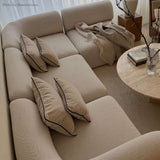 Cream Scandinavian corner sofa with soft cushions and a fringed throw beside a round coffee table in a warm neutral living room by sackit