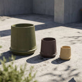 Three fluted frost resistant outdoor planters in olive green brown and sand tones displayed on a sunlit concrete terrace by sackit