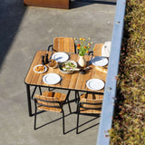 Outdoor teak dining set with four wooden chairs arranged around a table set for a meal on a sunny patio by sackit