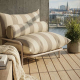 Striped bolster and seat cushions in neutral tones on a wooden outdoor lounge chair beside a potted plant with a waterfront view by sackit Europe