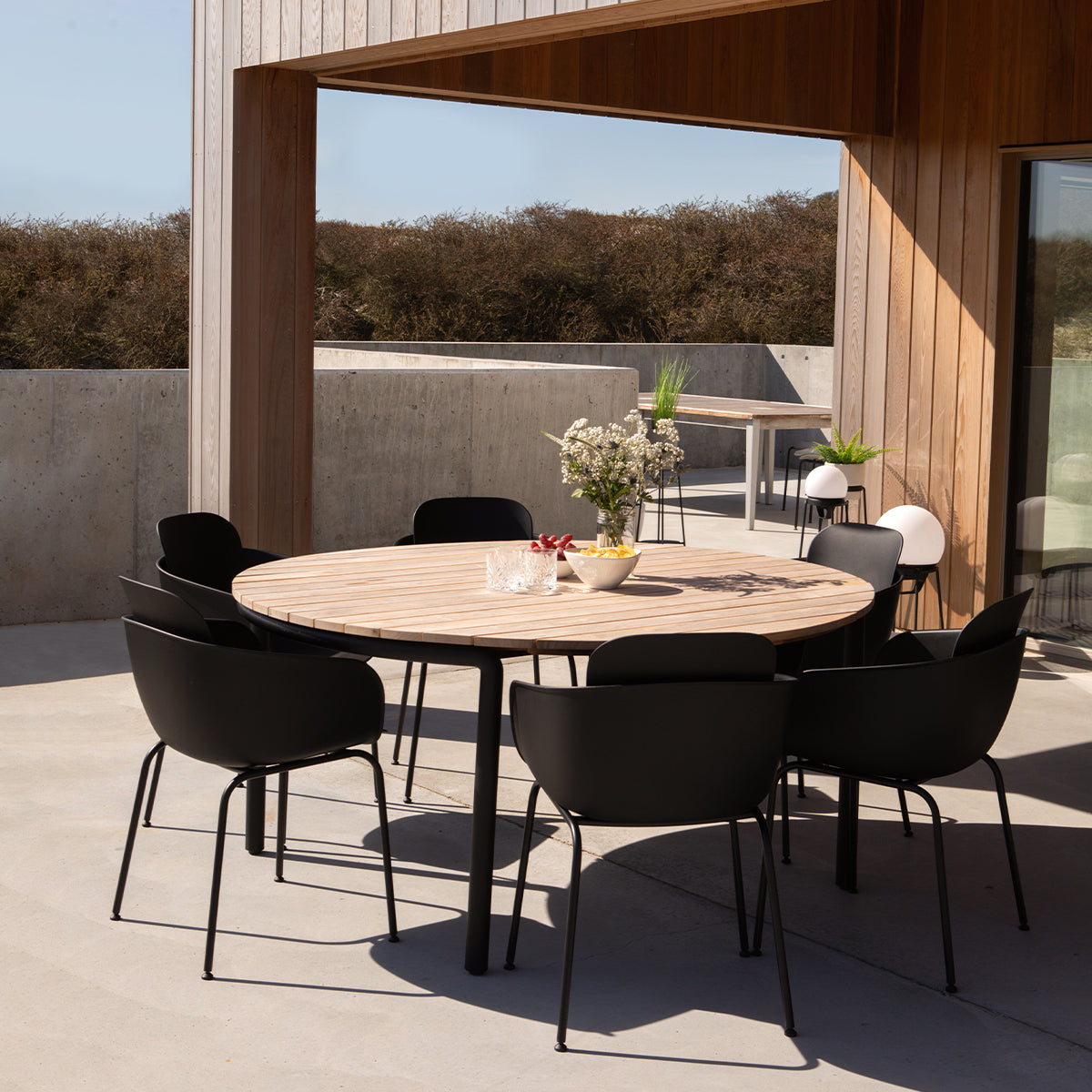 Round outdoor dining table with powder-coated aluminum legs and teak wood tabletop