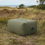 Olive green outdoor pouf from sackit europe set in a coastal meadow with grasses and wildflowers serving as a footrest or extra seat