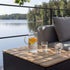 Outdoor storage coffee table with a slatted wooden top beside a gray lounge sofa with pitcher and glasses overlooking a calm lake from sackit