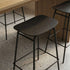 Black wood bar stool with a rounded rectangular seat and slim metal frame beneath a wooden bar counter in a modern indoor setting from sackit