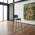 Black leather bar stool with a curved backrest and footrest in a modern room with wood flooring and artwork by sackit