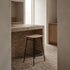 sackit wood bar stool with natural oak veneer seat and black metal frame in a warm brick kitchen interior