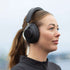 Woman wearing black sackit over ear headphones outdoors with a comfortable padded design and sleek modern styling