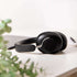 Black sackit over ear headphones resting on a white desk beside green leaves in a bright minimalist interior