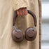 Brown over ear headphones held by a person in a beige coat showing padded ear cups and an adjustable headband from sackit