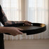 Person holding a round black lacquered serving tray from sackit for practical Nordic style dining and entertaining in a bright home interior