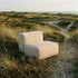 sackit outdoor lounge seat in soft cream fabric nestled among coastal dunes and beach grass with a sandy path under open skies