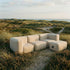 Cream sackit Soft Sofa Outdoor three seater sofa with matching pouf set among coastal dunes and tall grass under an open sky