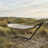 sackit Cobana hammock with cream fabric and black stand resting among coastal dunes beside the sea on a calm Nordic day
