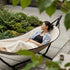 Woman relaxing in a Cobana hammock on a garden patio surrounded by lush greenery with a cup of coffee nearby