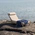 sackit Kirra sunbed with beige cushions and navy blanket resting on a rocky shore beside calm water outdoors