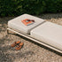 Kirra sunbed with beige cushions book and sandals on a gravel patio beside lush greenery from sackit