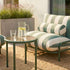 Outdoor sofa with a striped bolster cushion beside a round green table on a sunny terrace