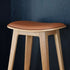 Nordic bar stool in terra black leather with oak wood and cross-stitching detail, 73 cm height.