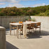 Outdoor ceramic dining table with six wooden chairs on a sunny concrete terrace surrounded by greenery from sackit in Denmark