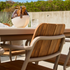 sackit outdoor dining chair with warm wooden slats and cream frame beside a matching table on a sunlit patio with glassware and greenery