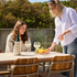 sackit outdoor dining set with a light ceramic table and wooden patio chairs styled with wine glasses fruit and two women outdoors