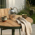 Round outdoor café table with teak wood top and powder-coated aluminum base in natural setting