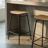 Bar stool with oak veneer seat and black powder-coated steel frame in a simple indoor setting