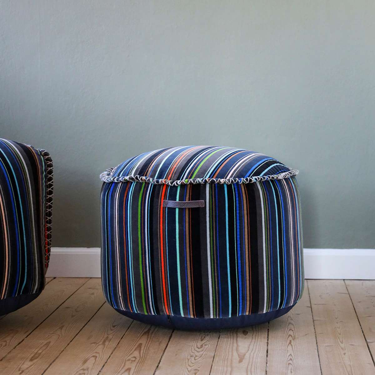 Round pouf with multi-colored linear Paul Smith cotton upholstery on a white background.
