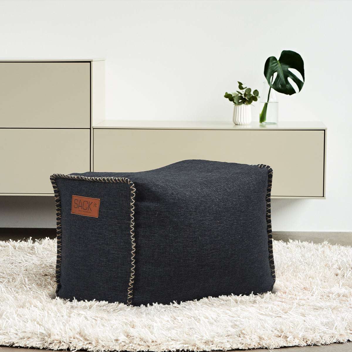 Black Cobana Square Pouf with canvas fabric and hand-sewn stitches in a simple setting