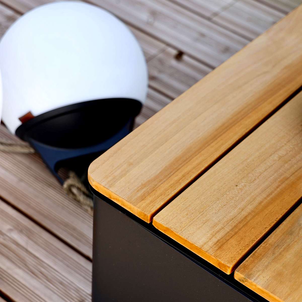 Black aluminum and teak Patio Storage Table with built-in storage, shown in outdoor setting next to sofa
