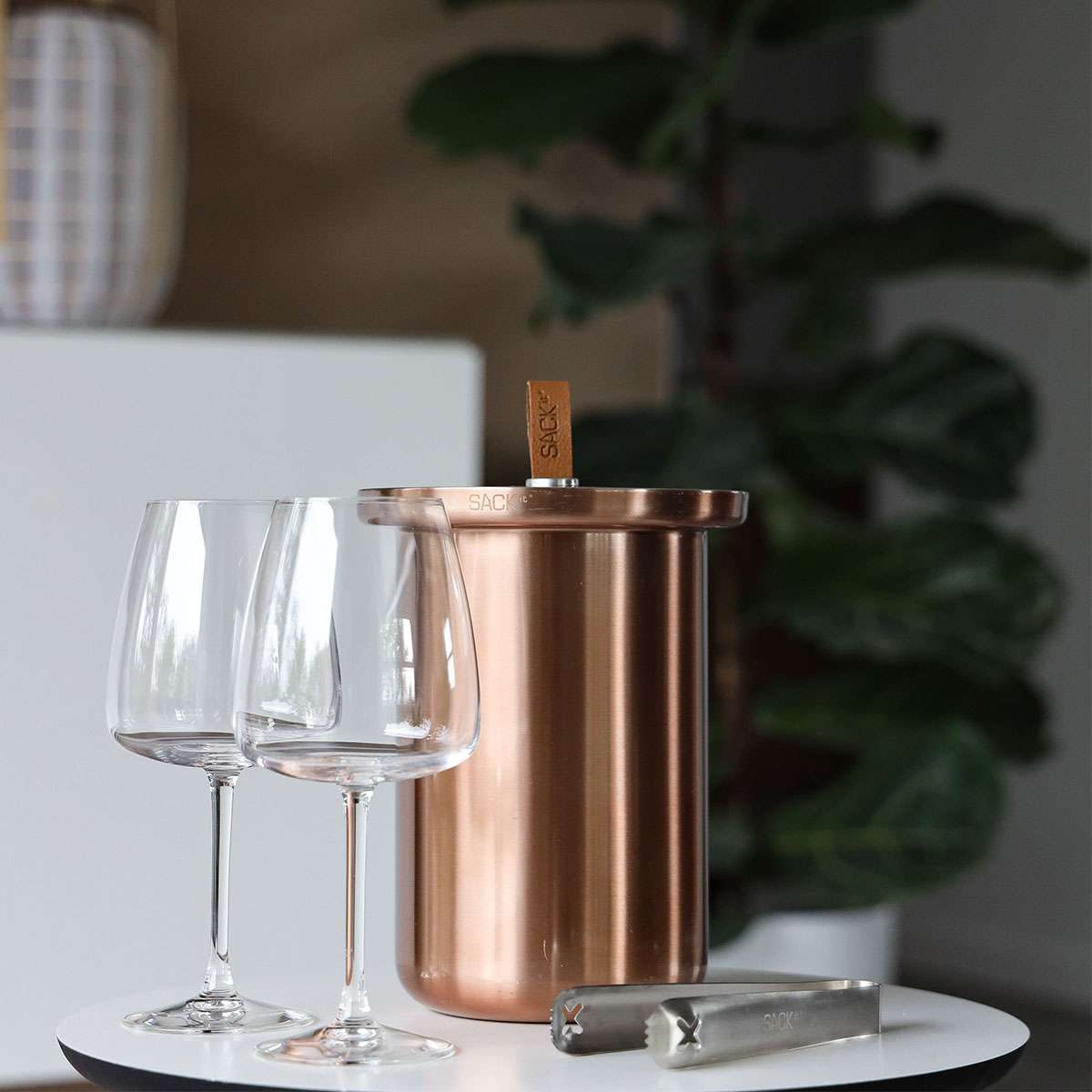 Copper-colored satin polished stainless steel wine cooler with leather handle and included ice tong on a white background.