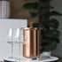 Copper-colored satin polished stainless steel wine cooler with leather handle and included ice tong on a white background.