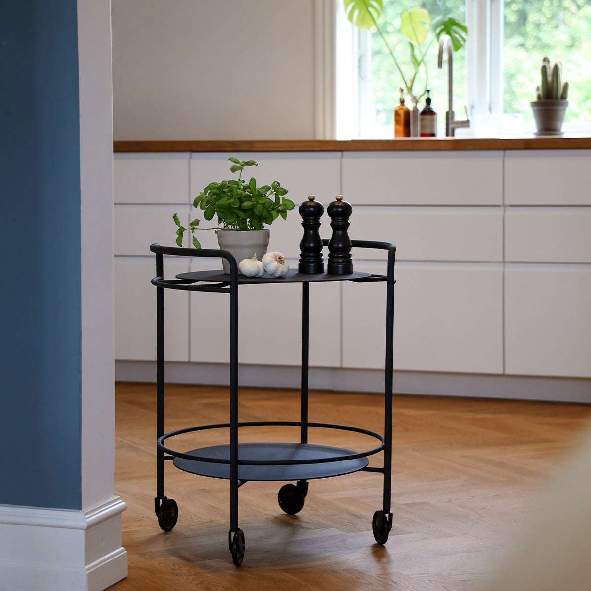 Matte black powder-coated steel Serving Table with four wheels and minimalist design on wooden floor.
