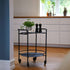 Matte black powder-coated steel Serving Table with four wheels and minimalist design on wooden floor.
