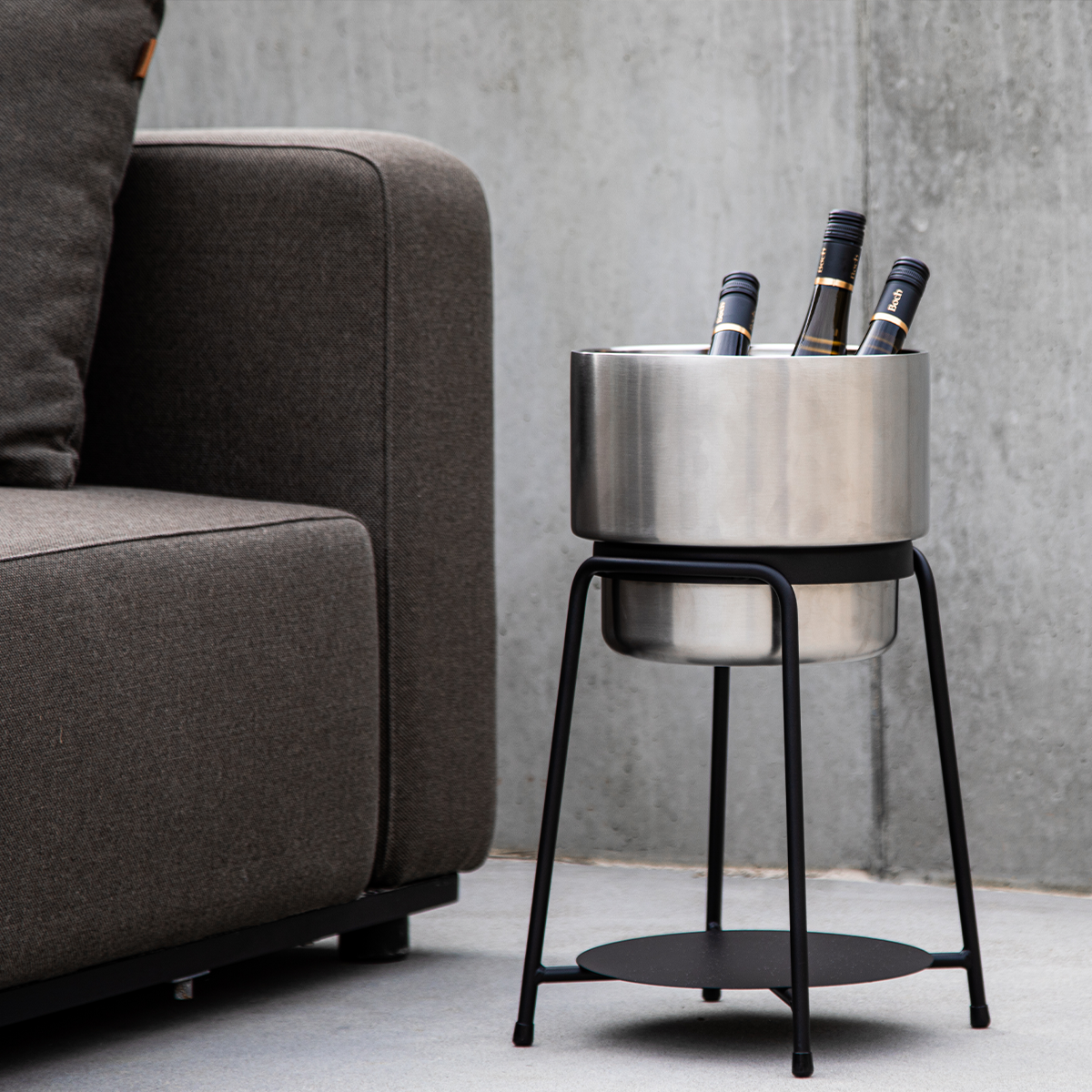 Black powder-coated stainless steel patio accessory stand with a stainless steel wine bucket and accessories on a wooden deck.