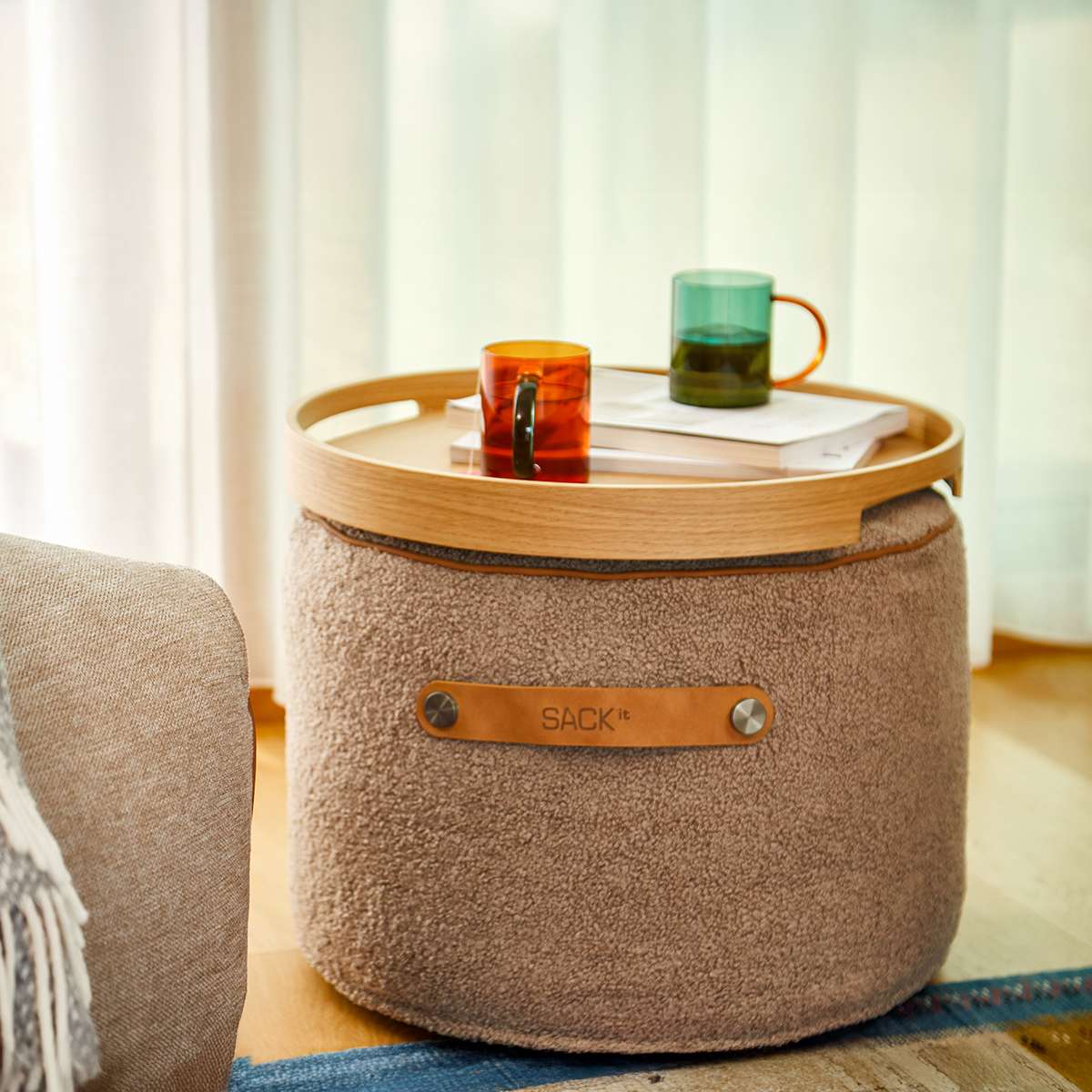 Round Teddy Brown SACKit Pouf Indoor with cold foam filling and PU leather side handle on a light floor.