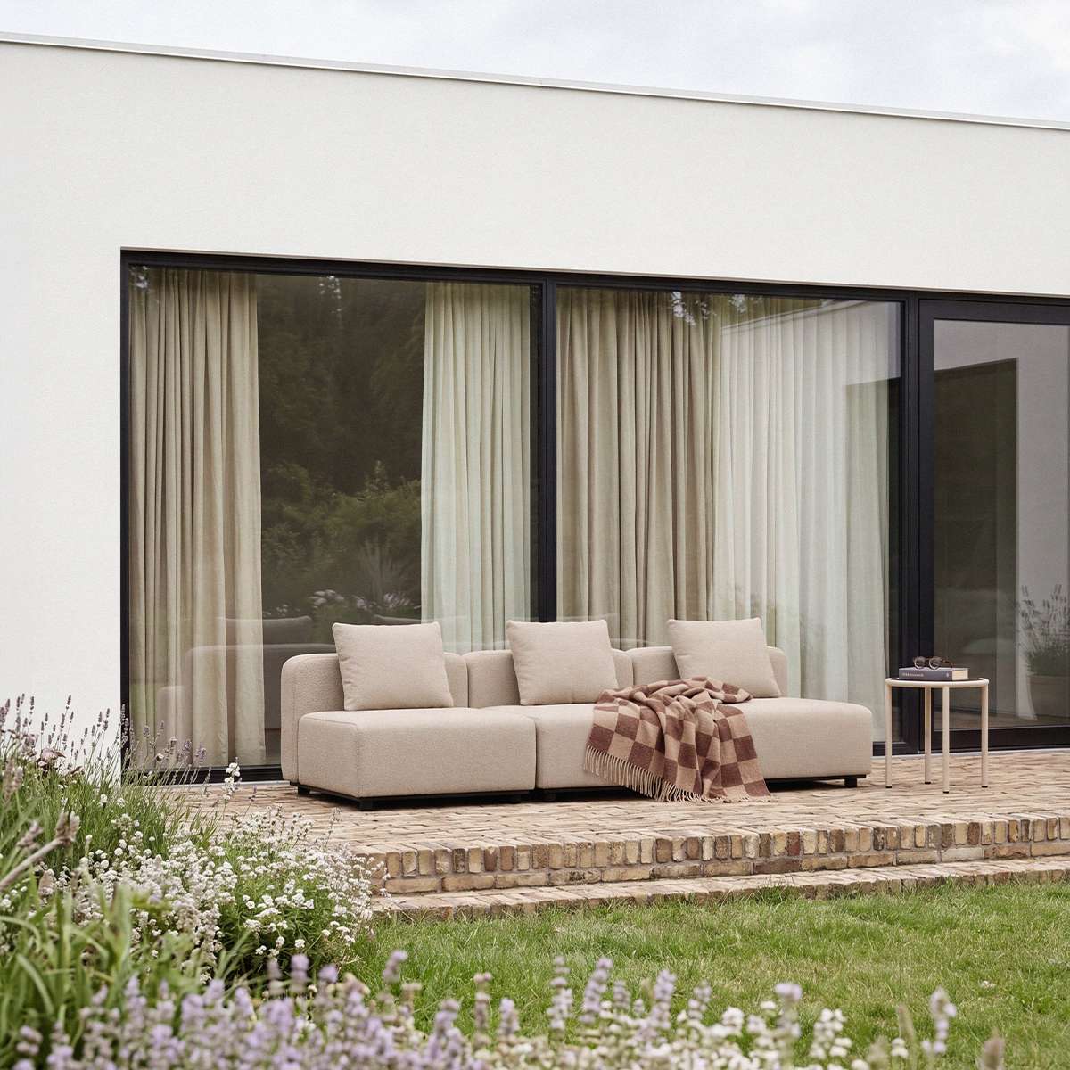 sackit Cobana three seater outdoor lounge sofa on a modern terrace with neutral cushions and a checked throw overlooking a landscaped garden