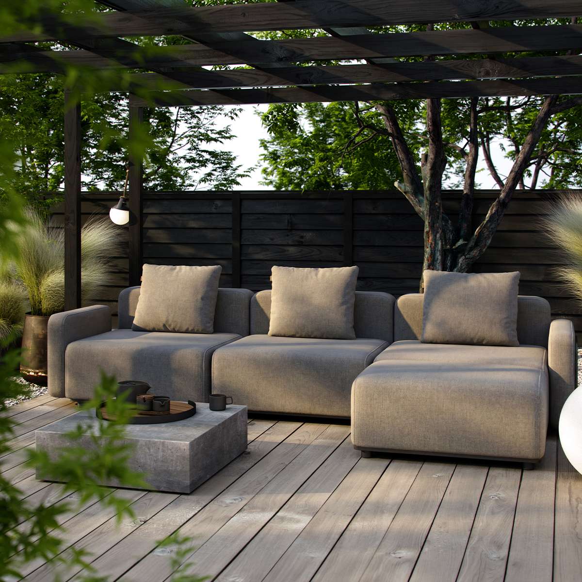 Outdoor three seat lounge sofa in warm gray with cushions on a timber deck beneath a pergola in a leafy garden designed by sackit