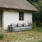 Gray three seat outdoor lounge sofa with modular cushions beside a rustic cottage in a natural garden setting by sackit