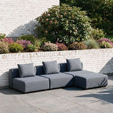 Dark gray three seat modular outdoor lounge sofa with cushions on a paved terrace beside a landscaped garden designed in Denmark by sackit