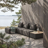 sackit dark modular outdoor lounge sofa with cushions and striped throw on a wooden coastal deck beside the sea and a pine lined Scandinavian cabin