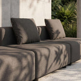 sackit Cobana three seater outdoor lounge sofa in dark grey with plush cushions beside a concrete wall and leafy garden