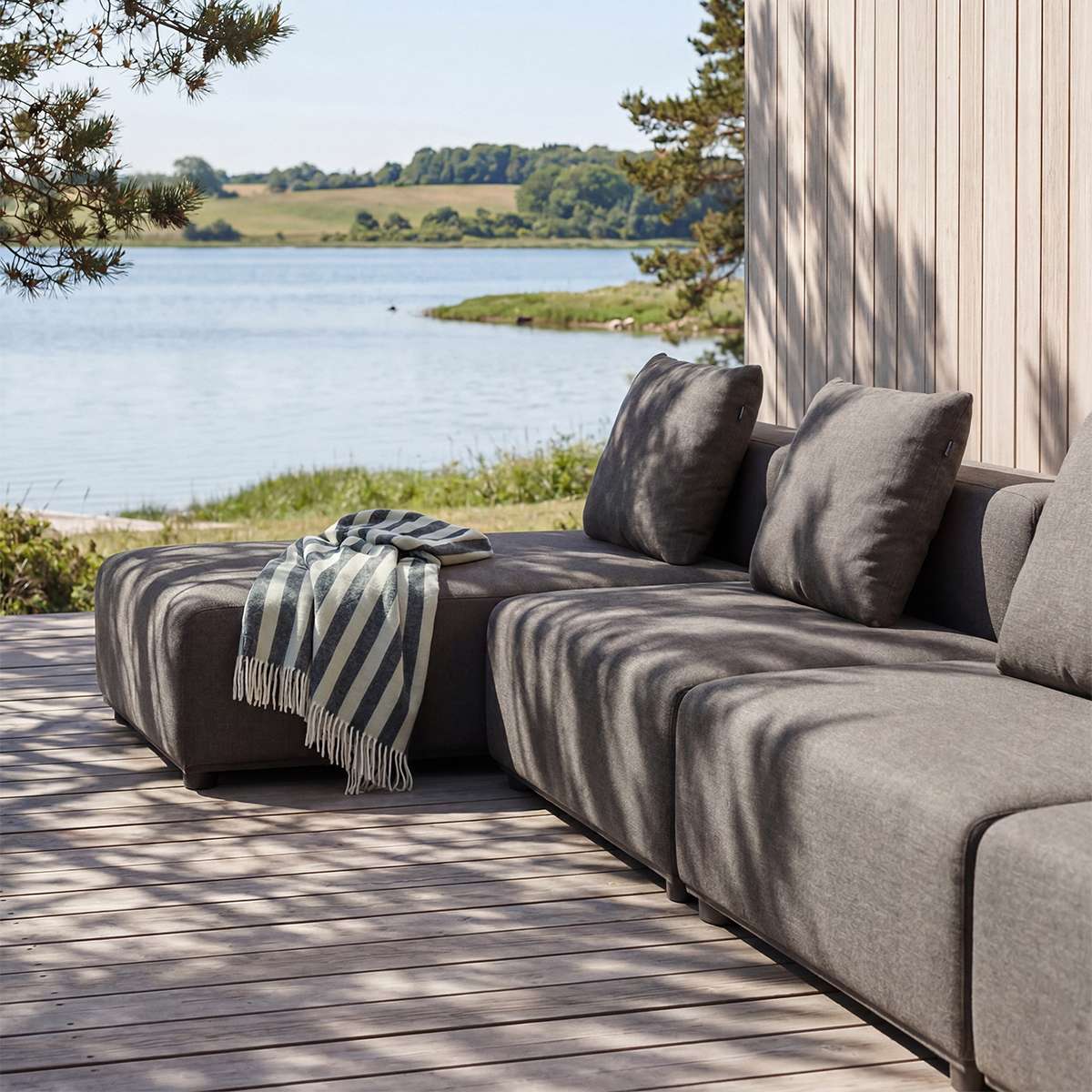 sackit Cobana outdoor lounge sofa in charcoal fabric with chaise and striped throw on a wooden terrace overlooking a calm Nordic lake